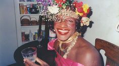 a woman with flowers on her head is holding a wine glass and smiling at the camera