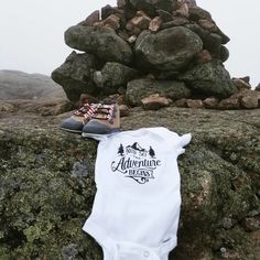 a baby's bodysuit and shoes are sitting on top of a rock formation