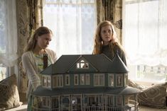 two women standing in front of a doll house