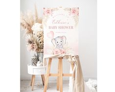 a baby shower sign sitting on top of a stool next to a vase with flowers