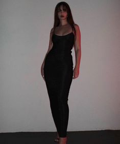 a woman standing in front of a white wall wearing a black dress and high heels