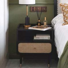 a nightstand with a lamp and books on it next to a bed in a bedroom