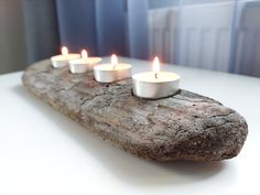 five lit candles sitting on top of a piece of driftwood in front of a window