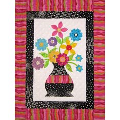 a vase filled with colorful flowers sitting on top of a wall hanging quilted in pink and black stripes