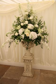 a vase filled with white flowers sitting on top of a wooden floor next to a curtain