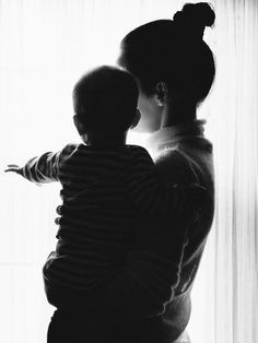 a woman holding a child in front of a window