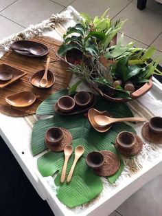 a table topped with lots of wooden spoons and bowls filled with green leafy plants