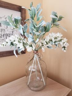 a vase filled with white flowers on top of a wooden table next to a framed sign