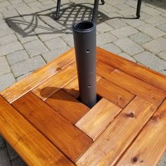 a square wooden table sitting on top of a brick floor next to a metal pole