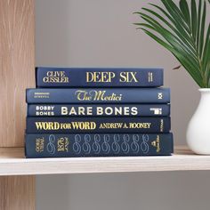 a stack of books sitting on top of a wooden shelf next to a potted plant