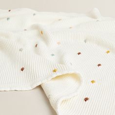 a white sweater with multicolored dots on the front and back, laying flat