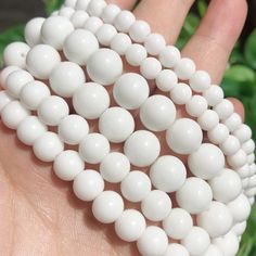 several white beads are being held in someone's hand with green plants behind them