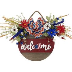 a patriotic welcome sign hanging on a wall with flowers and an american flag decoration in the center