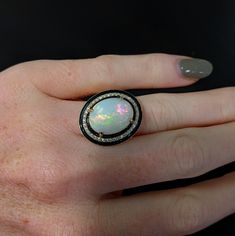 This statement ring features a 7.49 carat oval opal gemstone of size 16x12 mm with a halo of natural earth mined diamonds and black enamel detail, all set in solid 14K gold. This ring can be a beautiful October birthstone gift for your loved ones! This ring is made with solid 14K Gold and natural Earth mined SI / G-H diamonds. As listed, this ring is ready to ship. If you're interested in purchasing this setting with a different center stone please message us! Oval Cabochon Opal Ring In Fine Jewelry, Fine Jewelry Oval Opal Ring With Polished Finish, Oval Cabochon Opal Ring Fine Jewelry, Oval Opal Ring With Polished Finish In Fine Jewelry, Fine Jewelry Oval Cabochon Opal Ring, Oval Opal Ring With Polished Finish, Heirloom Oval Opal Ring Collectible, Oval Multi-stone Opal Ring Fine Jewelry, Fine Jewelry Oval Multi-stone Opal Ring