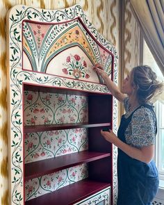 a woman in overalls painting a painted bookcase