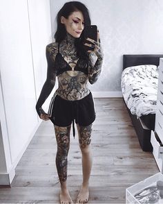 a woman with tattoos is taking a selfie in her bedroom while holding a cell phone