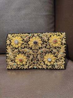 Beautiful hand-embroidered floral silk clutch bag inlaid with semi-precious stones. The front is completely covered in the design and has a closure flap with magnettic snap fastening. This clutch is perfect for daytime or night time. It is the ideal size for fitting all your essentials. It is a stylish accessory for each & every occasion. This equisite piece is even ideal for gifting to your near & dear one's . Thread - Silk Fabric - Velvet Variety of Semi-precious stones are used in this piece Zardozi is a type of heavy and elaborate metal embroidery on silk, satin, or velvet fabric base. Designs are often created using gold and silver wires and can incorporate pearls, beads, and precious stones. The embroidered silk clutch bag is made in Agra, India & is fully handmade. Designed to compl Traditional Embellished Clutch For Festivals, Elegant Embellished Embroidered Fabric For Festivals, Traditional Black Clutch With Handwork, Traditional Embellished Evening Bag For Festivals, Traditional Embellished Evening Bag For Festive Occasions, Formal Embroidered Clutch For Festivals, Rectangular Clutch With Gold Embroidery For Festivals, Rectangular Gold Embroidery Clutch For Festivals, Rectangular Gold Embroidered Clutch For Festivals