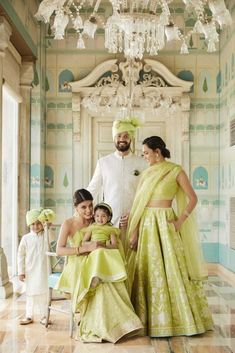 a man standing next to two women and children in green dresses with chandelier