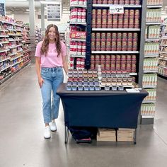 a woman standing next to a table with canned food on it in a grocery store