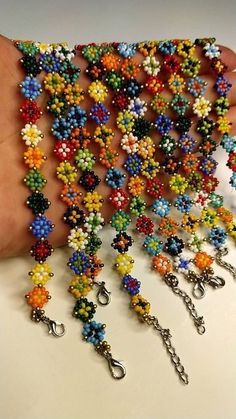 a hand is holding several bracelets made out of beads and chains, all in different colors