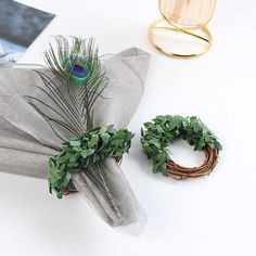 a white table topped with two wreaths next to a napkin and a peacock brooch