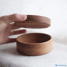 a person is holding their finger over a wooden box on a white surface with the lid open