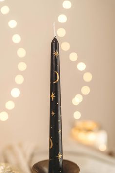 a black candle with stars and the moon on it sitting in front of some lights