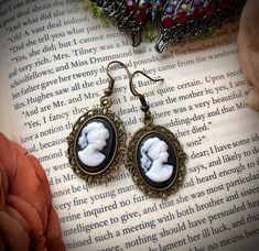 Inspired by the elegant style of early Nineteenth-century England, these beautifully hand-made dangle earrings are lightweight and the perfect accessory for any outfit! The pretty but simple cameo setting allows them to be worn with casual or formal attire.  Earring characteristics: -Metal Antique Brass French hook -Rubber earring back for extra security  -Black Resin Cameo Charms -Drop length: 1.25 inches  See the beautiful matching necklace here, which can be personalized: https://etsy.me/3bLh Blue Beaded Bracelets, Cameo Earrings, Gorgeous Bracelet, Formal Attire, Matching Necklaces, Blue Earrings, The Pretty, Earring Backs, Light Purple