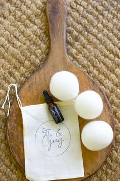 three balls of wool sit on top of a wooden board next to a bottle of essential oils