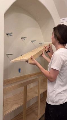 a woman standing in front of a shelf holding a piece of wood to the ceiling