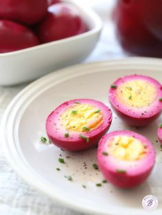 three deviled eggs on a plate next to a bowl of cherries in the background