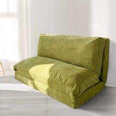 a green couch sitting on top of a hard wood floor next to a white wall