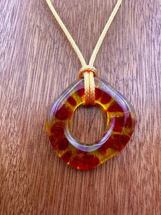 an orange and yellow glass pendant on a wooden table next to a string with a cord