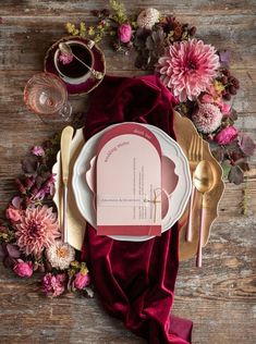 a place setting with red velvet napkins and gold cutlery on a wooden table