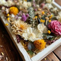 an arrangement of flowers on a white tray sitting on a wooden table with dried petals