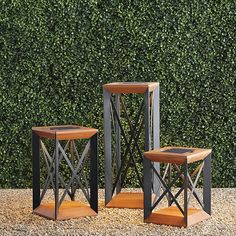 three wooden and metal side tables in front of a hedge