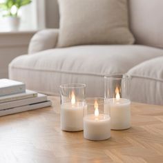 three lit candles sitting on top of a wooden table next to a book and couch