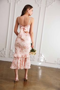 the back of a woman wearing a pink dress with flowers on it, standing in front of a white wall