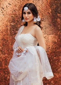 a woman in a white dress with flowers on her head standing next to a brick wall