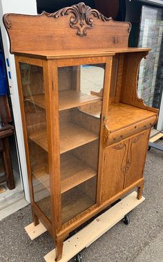 an old wooden cabinet with glass doors on wheels