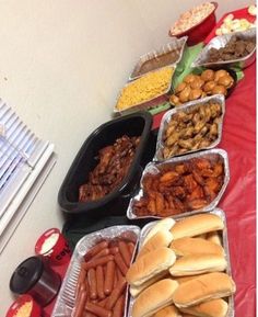 a table topped with lots of trays filled with hot dogs and other food items