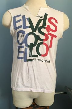 "Vintage 1980s off-white Elvis Costello and the Attractions \"Goodbye Cruel World USA Tour 1984\" t-shirt. Size: Adult Small (approximate - no tag) 50% polyester, 50% cotton The shirt is very soft and in good vintage condition, with no stains - though both sleeves and neckline have been cut. Approximate measurements with garment laying flat (INCHES) : Length (from top of shoulder at collar seam to bottom) : 24\" Sleeve (from top of shoulder seam to cuff edge) : n/a Between Shoulder Seams : 15.5\ Cruel World, Tour Music, 80s Shirts, Elvis Costello, Digital Closet, Rock Concert, 80s Vintage, Gender Neutral, Adult Outfits