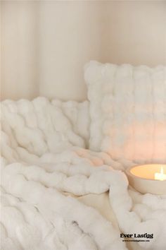 a candle is lit in the corner of a room with fluffy white blankets on it