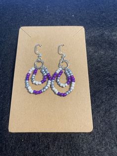 These double-looped drop earrings are accented with purple, white, and silver seed beads. Earrings are made of stainless steel wire with glass accents. Purple Metal Beaded Drop Earrings, Purple Teardrop Earrings With Dangling Beads, Purple Beaded Teardrop Earrings With Ear Wire, Purple Teardrop Beaded Earrings With Ear Wire, Purple Teardrop Beaded Earrings With Dangling Beads, Purple Teardrop Beaded Earrings, Adjustable Wire Wrapped Purple Beaded Earrings, Adjustable Purple Wire Wrapped Beaded Earrings, Purple Dangle Beaded Earrings Wire Wrapped