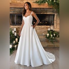 a woman standing in front of a fireplace wearing a white wedding dress with spaghetti straps