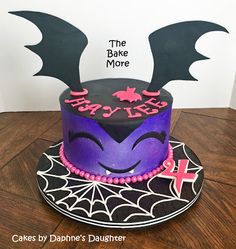 a cake decorated with purple and black icing on top of a wooden table next to a white wall