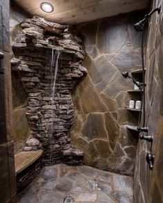 a bathroom with stone walls and a waterfall in the shower area, along with shelves on either side