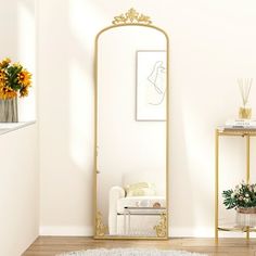 a white and gold living room with flowers in vases on the side table next to a mirror