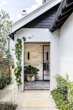 a white house with a black roof and some plants on the front door, along with a stone walkway