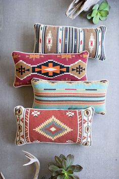 three decorative pillows on a wall with succulents and antlers in the background